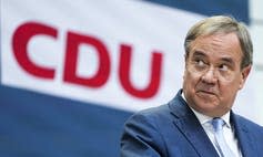 A man wearing glasses speaks with a CDU sign behind him.