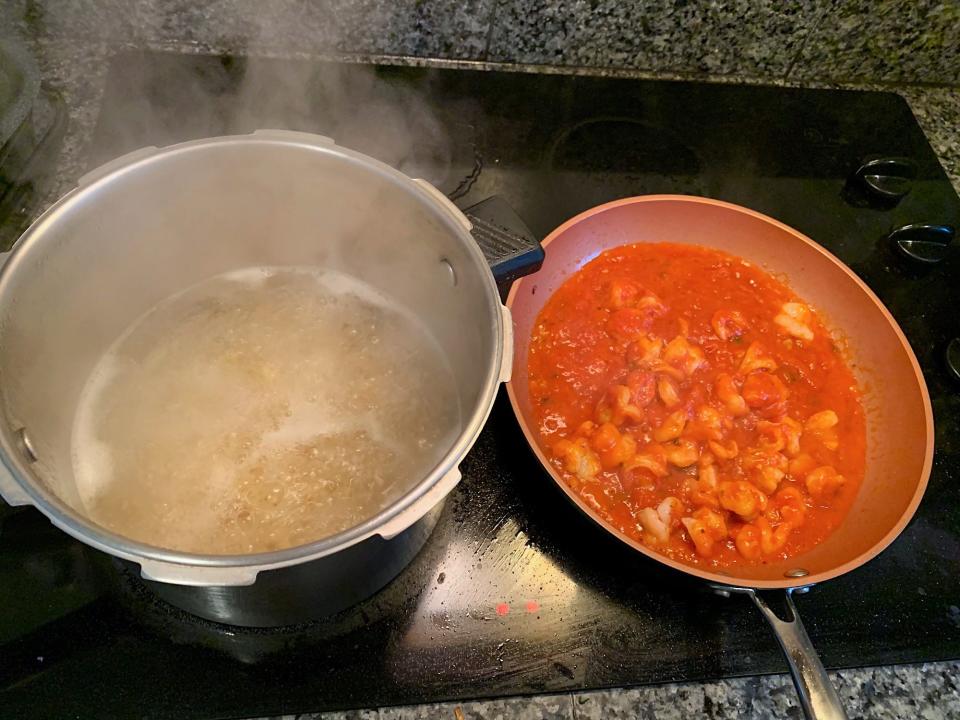 The pasta sauce and shrimp simmering next to pot with pasta cooking