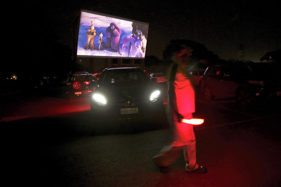 Un trabajador con linterna roja hace señales a los conductores en un autocine en Brasilia, 13 de mayo de 2020. (AP Foto/Eraldo Peres)