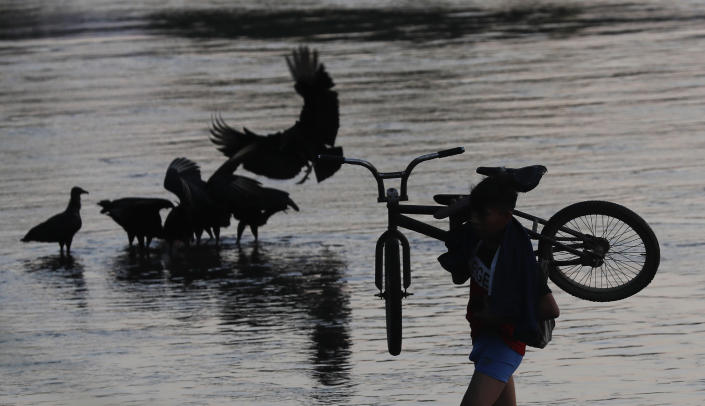 A local carries a bicycle in the Suchiate River, which creates a natural border between Mexico and Guatemala, near Ciudad Hidalgo, Mexico, Wednesday, Jan. 22, 2020, a location popular for migrants to cross from Guatemala to Mexico. The number of migrants stuck at the Guatemala-Mexico border continued to dwindle Wednesday as detentions and resignation ate away at what remained of the latest caravan. (AP Photo/Marco Ugarte)