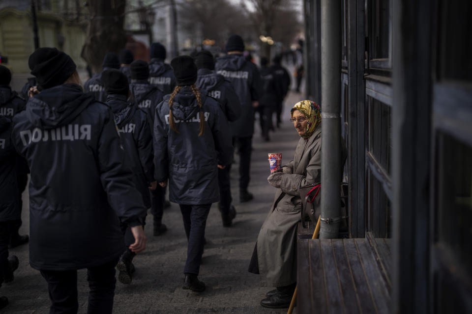 Ukrainian police officers march past a woman begging for alms during a demonstration in Odessa, Ukraine, Sunday, Feb. 20, 2022. Thousands of people in Odessa marched through the streets of the city in a show of unity on Sunday, marking the date on which, eight years ago, more than a hundred people were killed during Ukraine's Maidan revolution. Waving national flags and placards with slogans such as, 'No Putin, No Cry', people said they had come out to demonstrate against a potential Russian invasion, and said that they were prepared to defend their city if needed. (AP Photo/Emilio Morenatti)