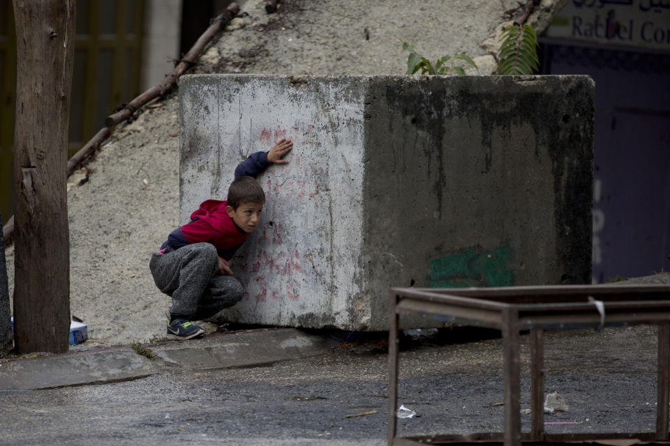 A Palestinian take cover during clashes with Israeli troops Monday, Dec. 9, 2019, in the West Bank city of Hebron. Palestinian residents of Hebron held a general strike on Monday, shuttering shops, schools and businesses to protest an Israeli plan to build a new Jewish neighborhood in the heart of the region's largest city. (AP Photo/Majdi Mohammed)