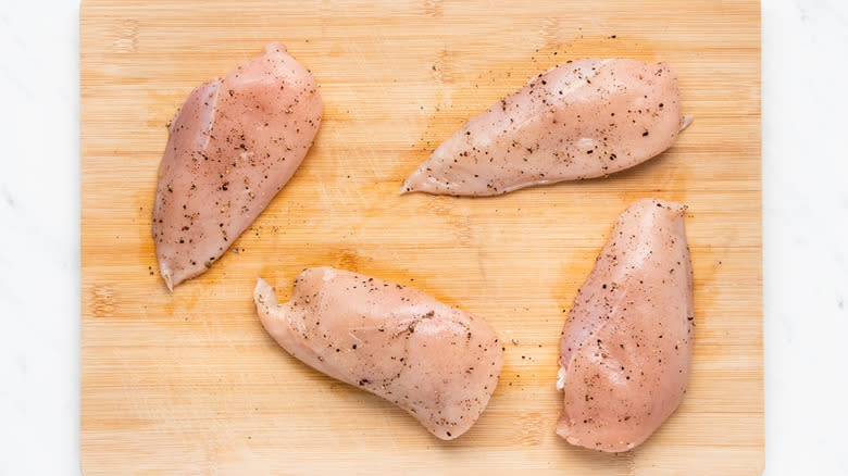 Seasoned chicken breasts on chopping board