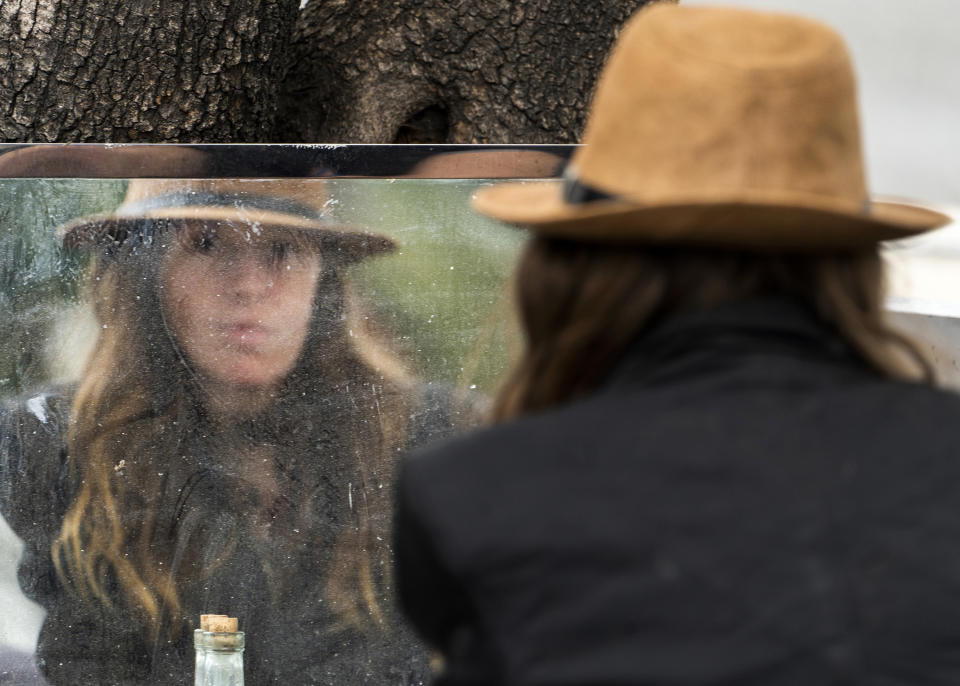 Dawn Woodward, 39, who is homeless and originally from Arizona, checks herself in the mirror set outdoors in a homeless camp on the side of the CA-101 highway in the Echo Park neighborhood in Los Angeles Tuesday, May 11, 2021. California Gov. Gavin Newsom on Tuesday proposed $12 billion in new funding to get more people experiencing homelessness in the state into housing and to “functionally end family homelessness” within five years. (AP Photo/Damian Dovarganes)