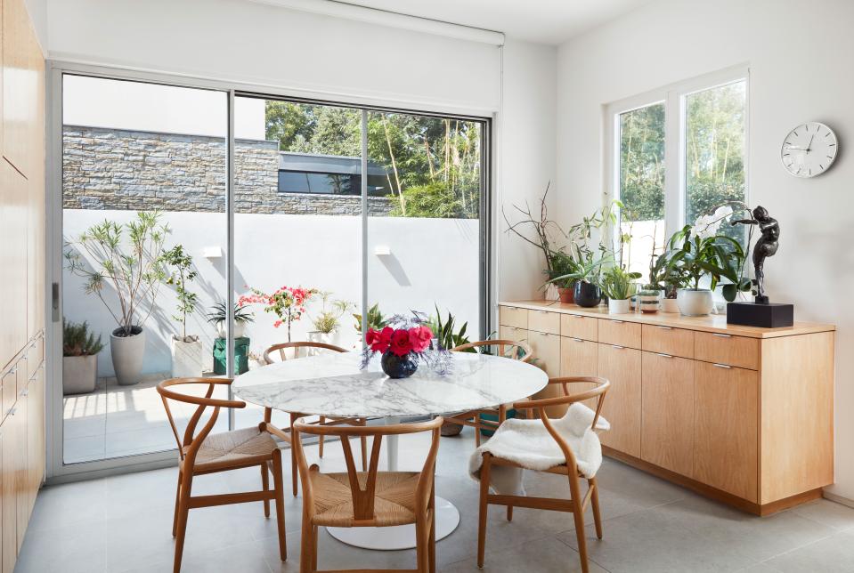 The couple kept to midcentury classics for the kitchen’s fuss-free dining  area: a Saarinen Tulip table surrounded by Wegner Wishbone chairs. The sliding doors lead to a patio where the couple grills.