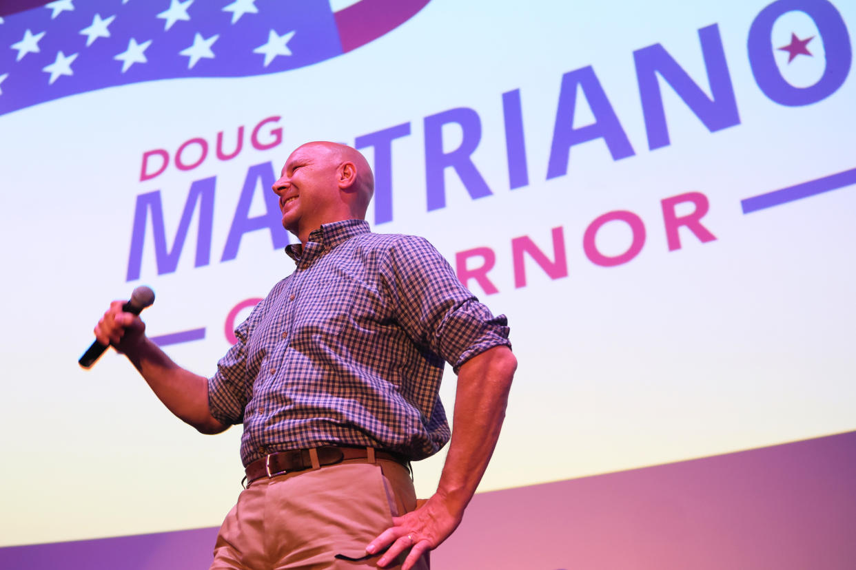 Doug Mastriano holds a microphone and stands in front of a backdrop that reads: Doug Mastriano for Governor.