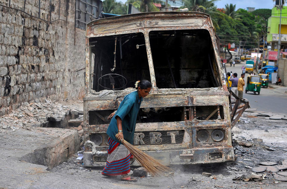 A municipal worker sweeps around the charred remains of a lorry set ablaze during the violent protests in Bengaluru