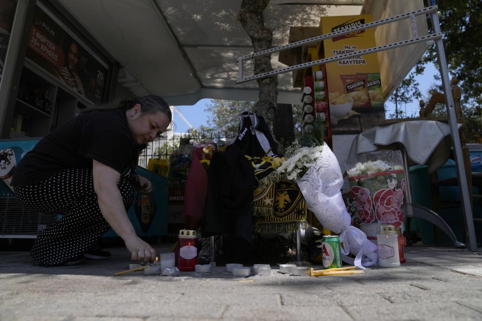 A woman lights a candle, on the location where a 29-year-old Greek fan has died after overnight clashes between rival supporters in Nea Philadelphia suburb, in Athens, Greece, Tuesday, Aug. 8, 2023. European governing soccer body UEFA says it has postponed a Champions League qualifying game between AEK Athens and Croatia's Dinamo Zagreb scheduled for Tuesday because of the violence. Eight fans were injured while Greek police said Tuesday they had made 88 arrests, mostly of Croatian supporters. (AP Photo/Thanassis Stavrakis)