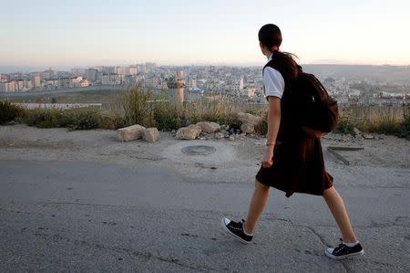 A Palestinian school gril walks to her school as Israeli Qalandiya checkpoint is seen behind the Israeli barrier near the West Bank city of Ramallah April 25, 2017. REUTERS/Mohamad Torokman