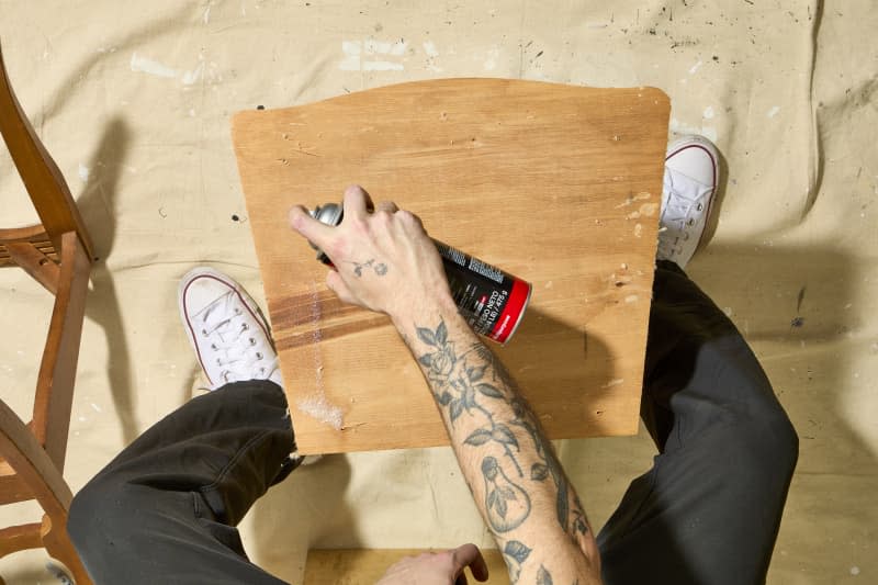 overhead shot of spray adhesive being applied to the bare wood seat.