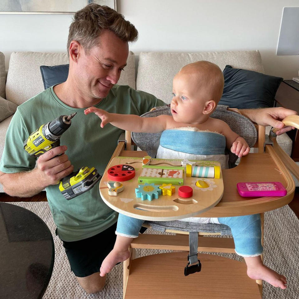 Grant Denyer pretends to show his baby Sunday how to use a drill while Sunday sits in a high chair. 