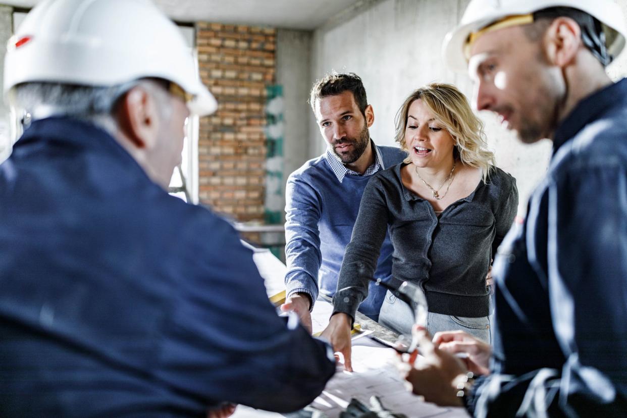 Young couple communicating with construction workers while analyzing housing plans during home renovation process.