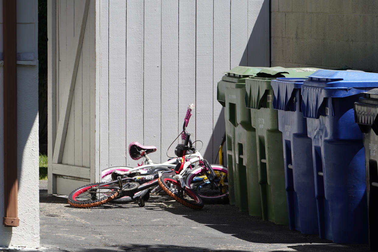 Childrens' bycicles are left near trash cans of a ranch-style house in the West Hills neighborhood of the San Fernando Valley, in Los Angeles, Monday, May 9, 2022. Police say three children were found dead at the home over the weekend and their mother and a teenager were arrested in the killings. (AP Photo/Damian Dovarganes)