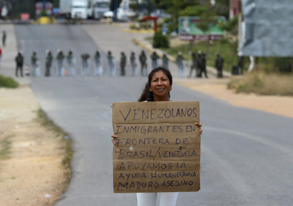 A Venezuelan holds a sign that reads in Spanish "Venezuelan migrants at the border between Brazil-Venezuela, we support the humanitarian aid. Maduro assassin" as she waits for the opening of the border in Pacaraima, Roraima state, Brazil, Friday, Feb. 22, 2019. Heightened tensions in Venezuela left a woman dead and a dozen injured near the border with Brazil on Friday, in the first deadly clash over the opposition's attempts to bring in emergency food and medicine that President Nicolas Maduro says isn't needed and has vowed to block. (AP Photo/Edmar Barros)