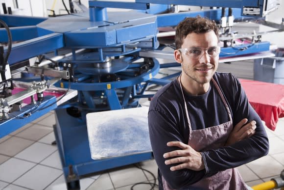 A young manufacturing worker posing in with his arms crossed in front of heavy-duty machinery.