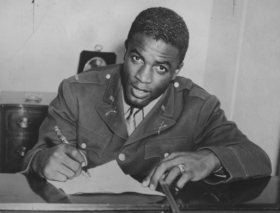 jackie robinson looking at a camera while signing papers