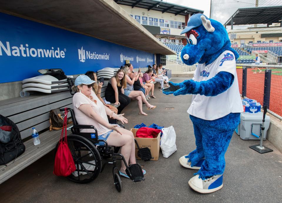 Blue Wahoos mascot Kazoo makes his way through the dugout to greet Amanda "Mandi" Furness at Blue Wahoos Stadium in Pensacola on Monday. The Gulf Breeze mother, who has been battling lupus and multiple sclerosis, decided to use her My Wish granted by Covenant Care to see her 10-year-old son, Hudson Furness, play baseball on the field at the stadium.