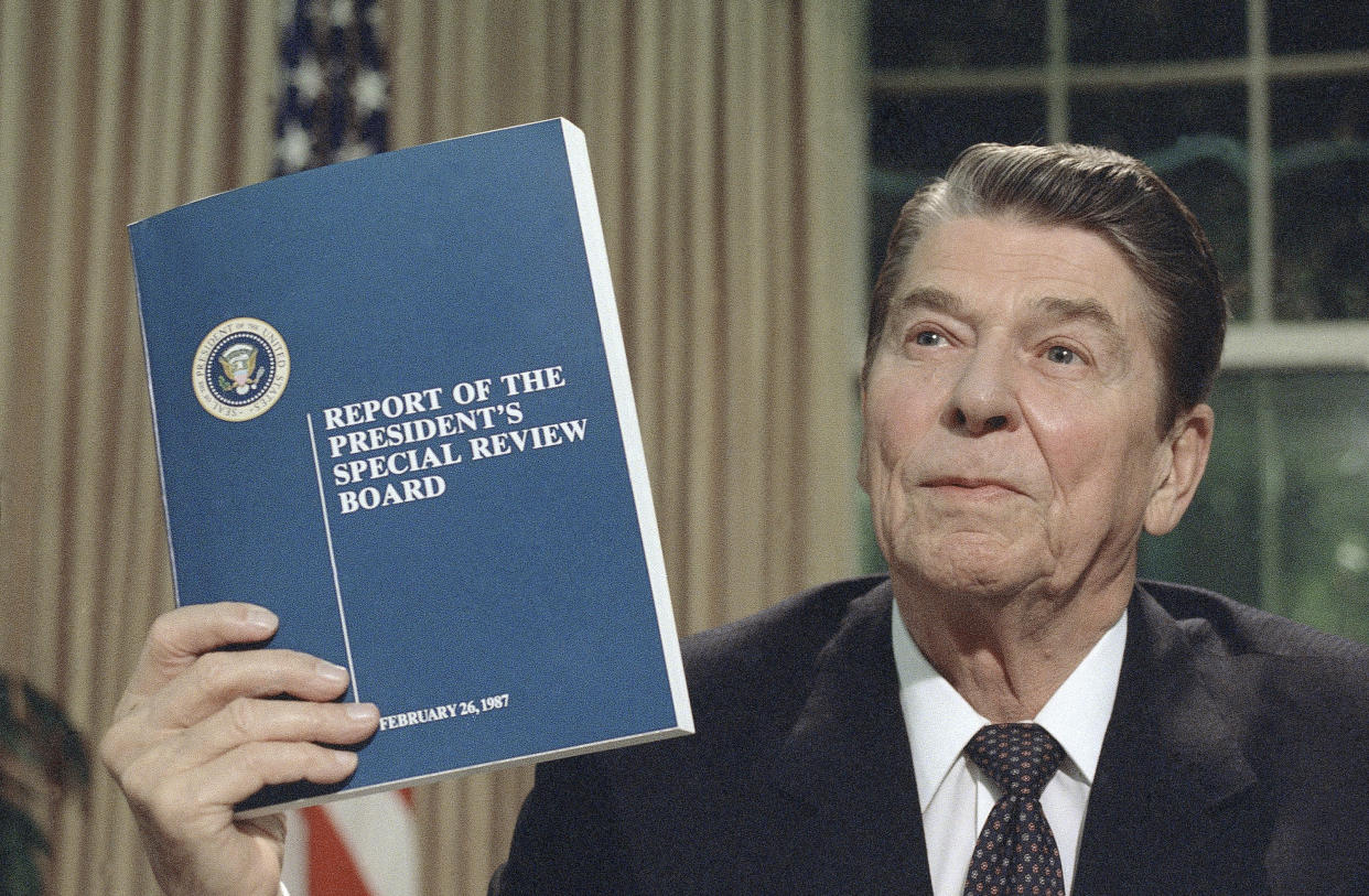 FILE - President Ronald Reagan holds up a copy of the Tower Commission report on the Iran-Contra affair, while posing for photographers after his nationally televised speech from the Oval Office in Washington, Aug. 13, 1987. Reagan said he was "mad as a hornet" about damage to his administration from the Iran-Contra affair. (AP Photo/Ron Edmonds, File)