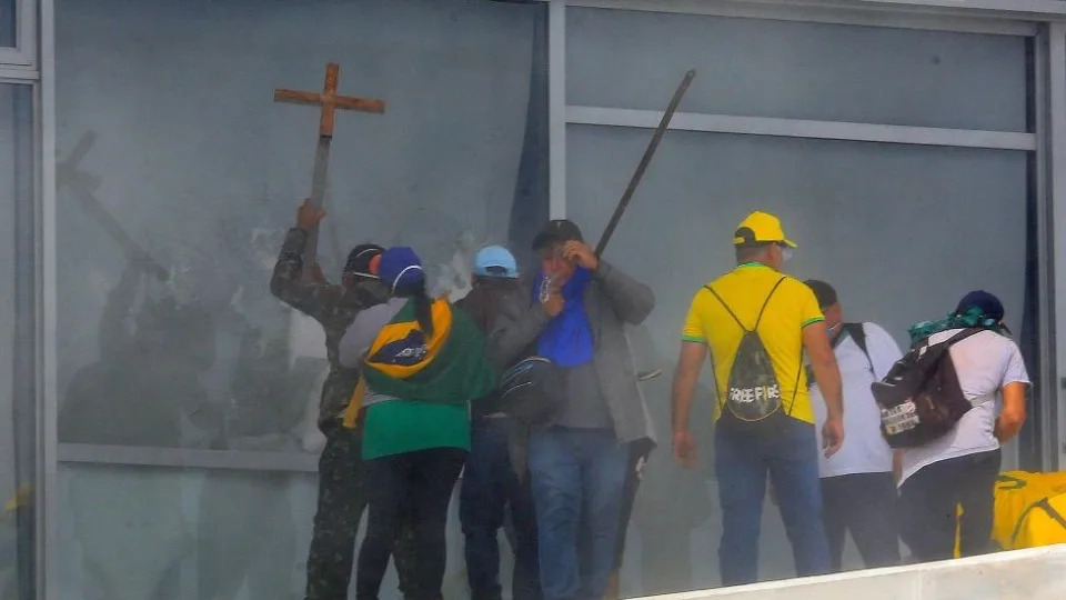 Manifestantes quebrando janelas ao invadir o Palácio do Planalto, protagonizando cenas que lembram a invasão do Capitólio dos EUA em janeiro de 2021