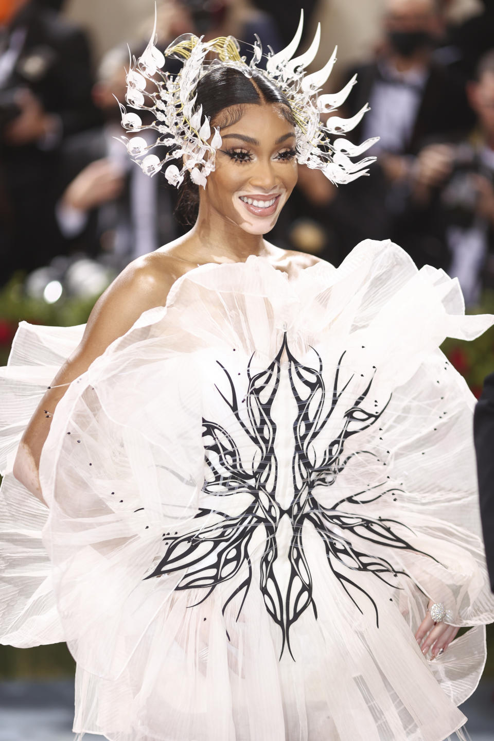 Winnie Harlow in a white dress and large white, feathery headpiece