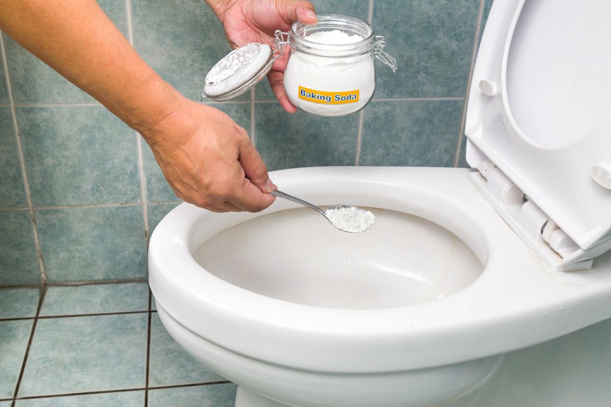 hands putting a scoop of baking soda in the toilet
