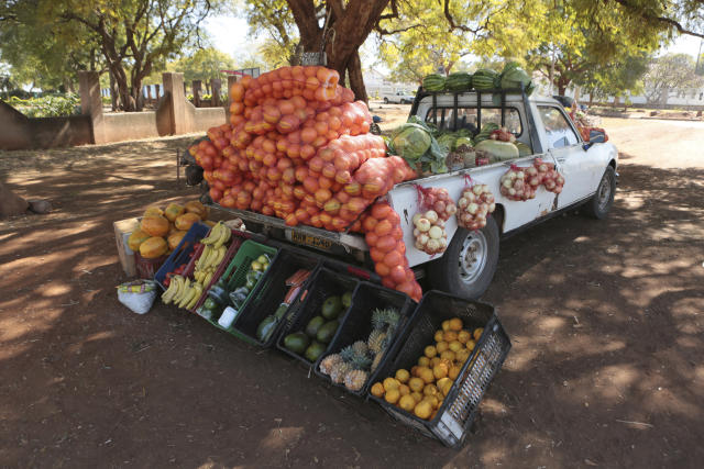 People sell clothes displayed on their car by the side of a busy