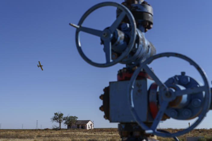 A crop dusting plane flies over a field next to an oil well in the Permian Basin in Lenorah, Texas, Friday, Oct. 15, 2021. Methane emissions are notoriously hard to track because they are intermittent. An old well may be wafting methane one day, but not the next. (AP Photo/David Goldman)