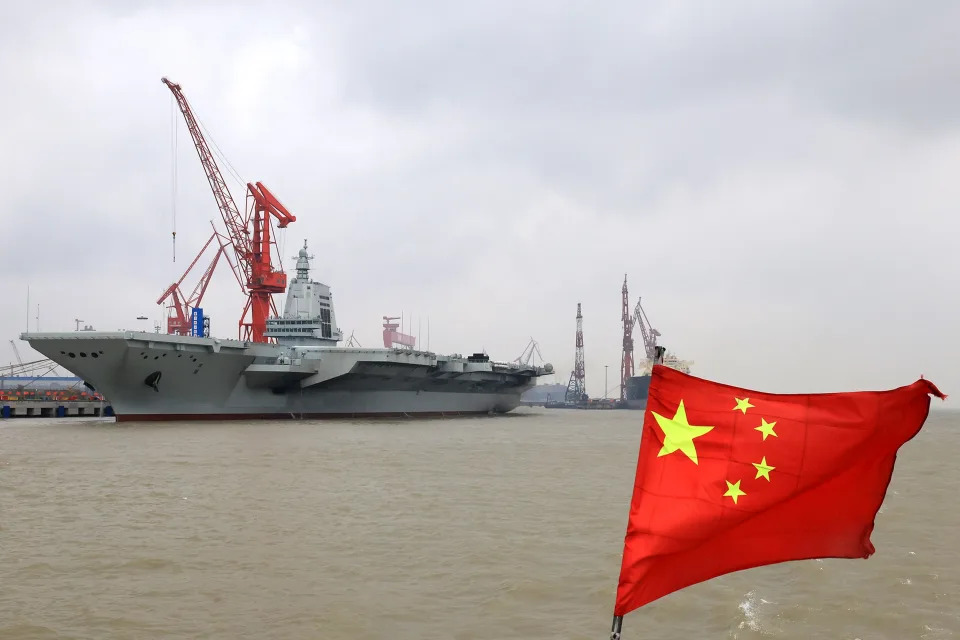 China's third aircraft carrier, the Fujian, docks in Shanghai with a Chinese flag seen in the foreground.