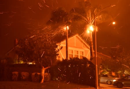 A local neighbor tries to fight a wind-driven wild fire called the Saddle Ridge fire with a garden hose in the early morning hours Friday in Porter Ranch