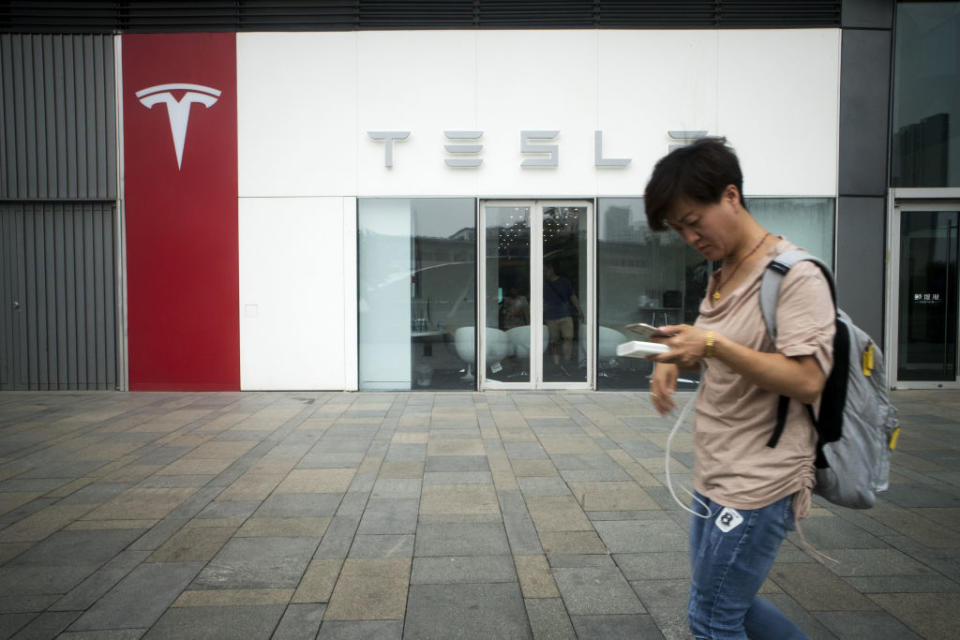 A pedestrian using a smartphone walks past a Tesla showroom in Beijing, China, on Saturday, July 7, 2018. (Giulia Marchi/Bloomberg)