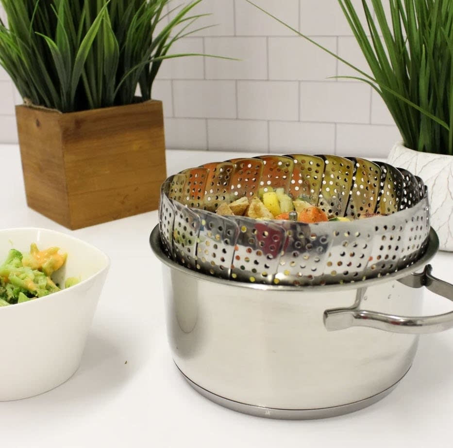 A steamer pot with vegetables on a kitchen counter next to a plant