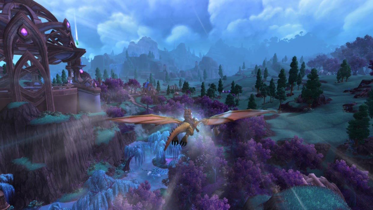  WoW 10.2.5 update - a player is dragonriding over a landscape with green fields and purple-leaved trees. 