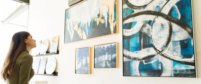 Side view of a beautiful young woman studying and watching the abstract paintings and colorful canvases during a visit to the art gallery