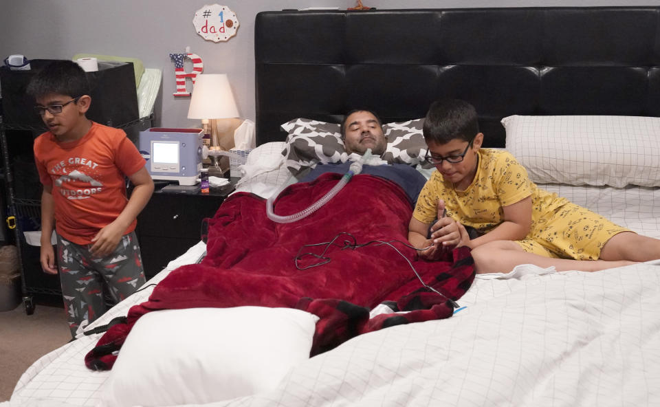 Keaton Koyita, 9, right, adjusts his father Rupesh Kotiya's hand as he and his brother Ronan Kotiya, 11, helped prepare him for bed at their home in Plano, Texas, Friday, April 8, 2022. Millions of Americans with serious health problems depend on children ages 18 and younger to provide some or all of their care at home. An exact number is hard to pin down, but researchers think millions of children are involved in caregiving in the U.S. (AP Photo/LM Otero)