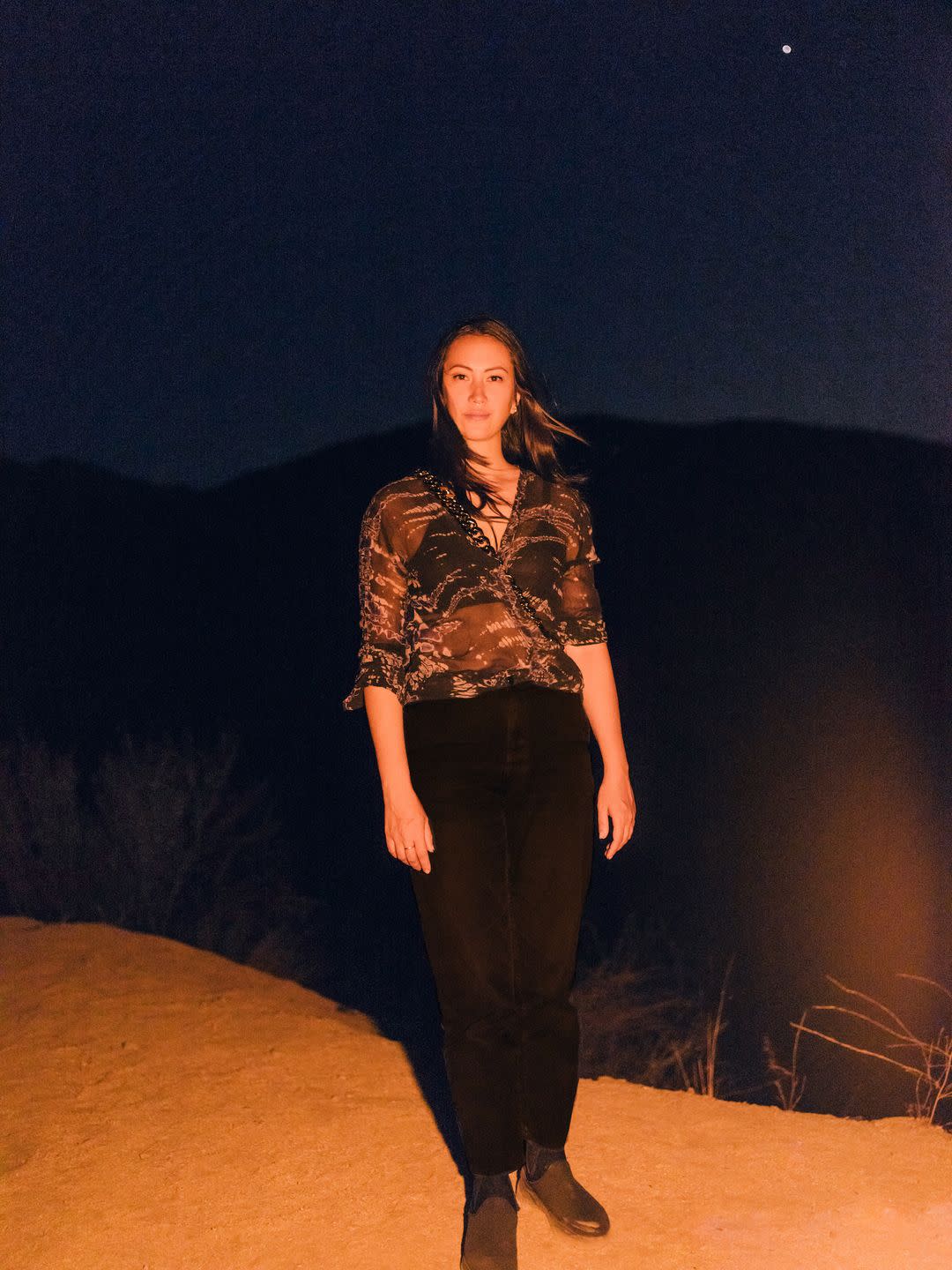 kara designer sarah law in a sheer printed top and black trousers standing outdoors at night
