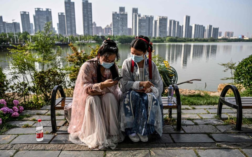 Young women wearing facemasks and traditional costumes of Song dynasty and Tang dynasty are seated on a bench in a park next to the East Lake in Wuhan - HECTOR RETAMAL /AFP