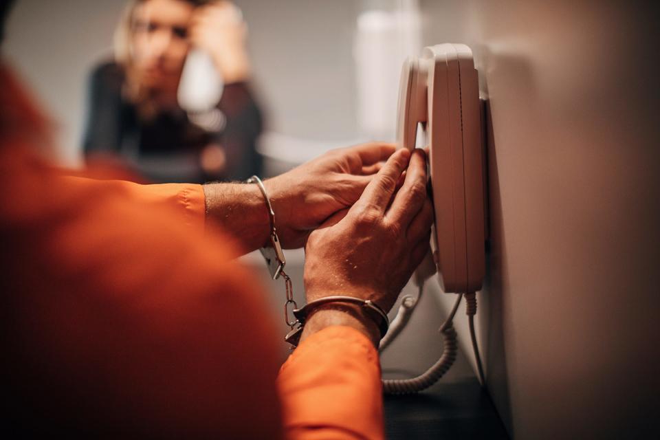 A prison inmate picking up the phone to talk to a visitor.