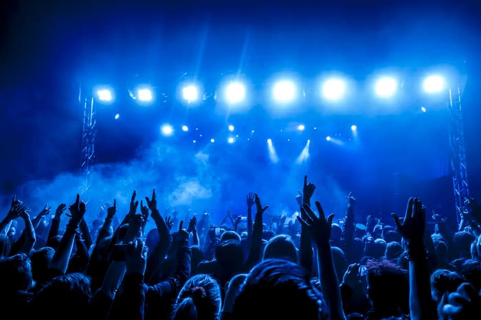 A large crowd cheering in front of a stage with beaming bright blue lights.