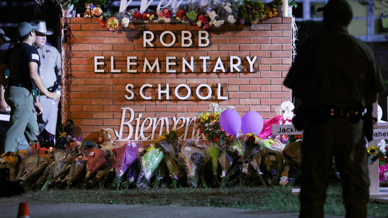 Flowers are placed on and next to a brick structure with a sign reading: Robb Elementary School.