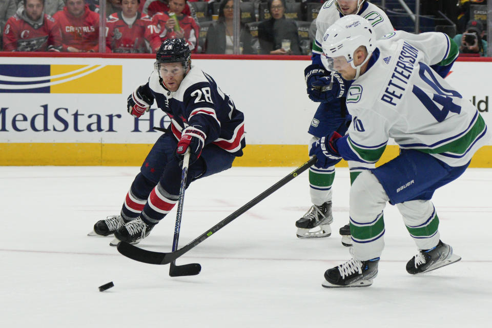 Washington Capitals right wing Connor Brown (28) and Vancouver Canucks center Elias Pettersson (40) reach for the puck during the first period of an NHL hockey game, Monday, Oct. 17, 2022, in Washington. (AP Photo/Jess Rapfogel)