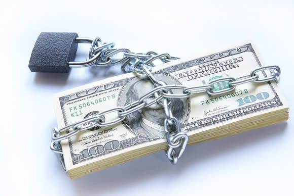 A stack of hundred dollar bills contained by chains and a lock.