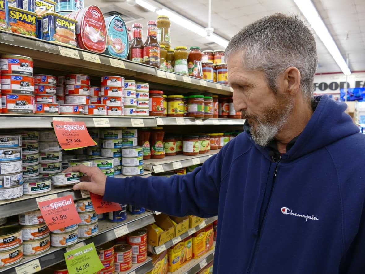 Todd Donohue looks at a can of tuna in a Winnipeg grocery store. The community advocate who receives employment and income assistance through the Manitoba government says the additional $25 he's receiving each month doesn't do enough to bring people on disability out of severe poverty. (Jeff Stapleton/CBC - image credit)