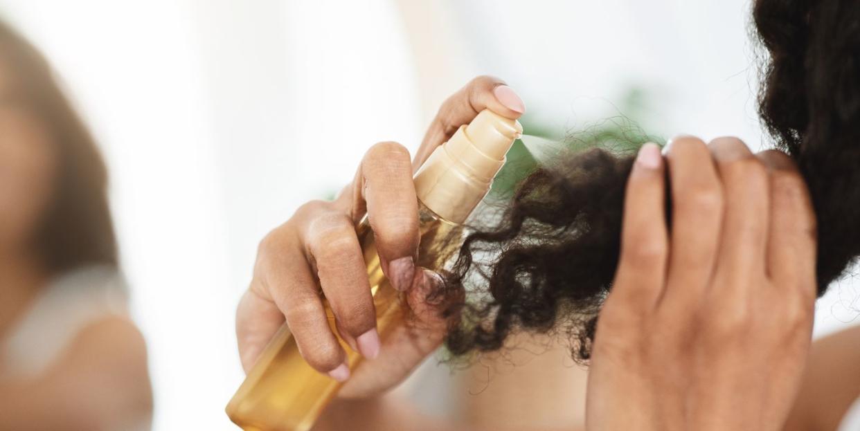 split ends remedy unrecognizable black woman applying moisturising spray to curly hair