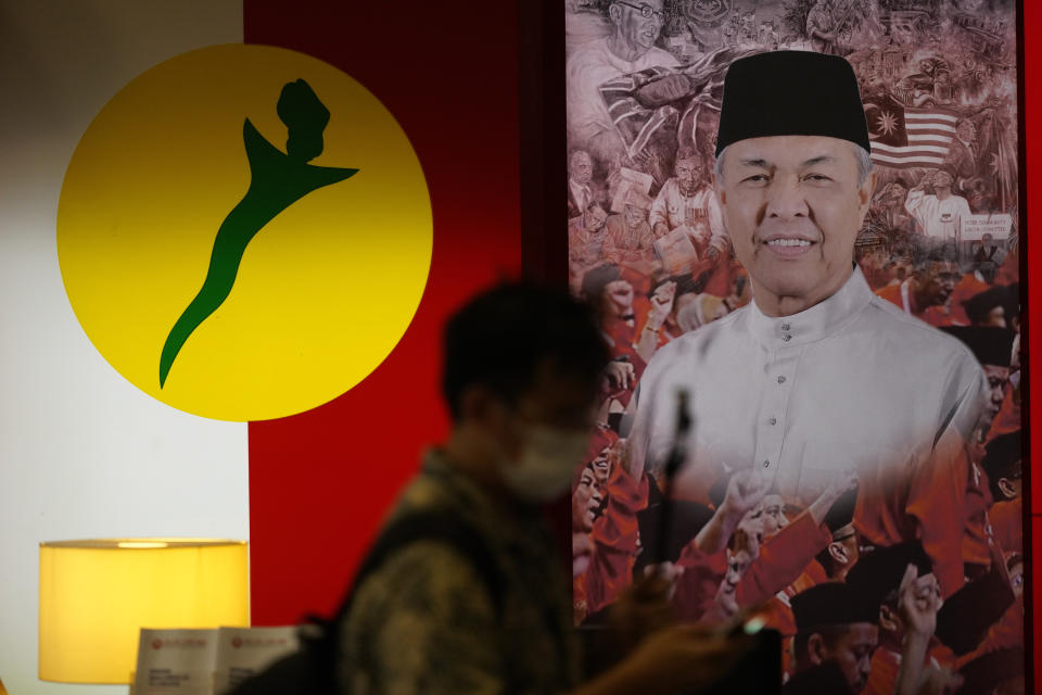 A man walks in front of a poster of UMNO ( United Malays National Organisation) President Ahmad Zahid at UMNO headquarter in Kuala Lumpur, Malaysia, Monday, Oct. 26, 2020. A key ally has reaffirmed support for Malaysian Prime Minister Muhyiddin Yassin's government, offering him a respite after his failed bid to declare a coronavirus emergency, but his political survival still hangs in the balance. The UMNO, the biggest party in the unelected governing coalition was angry at being sidelined amid rivalry with Muhyiddin's own Malay party. (AP Photo/Vincent Thian)