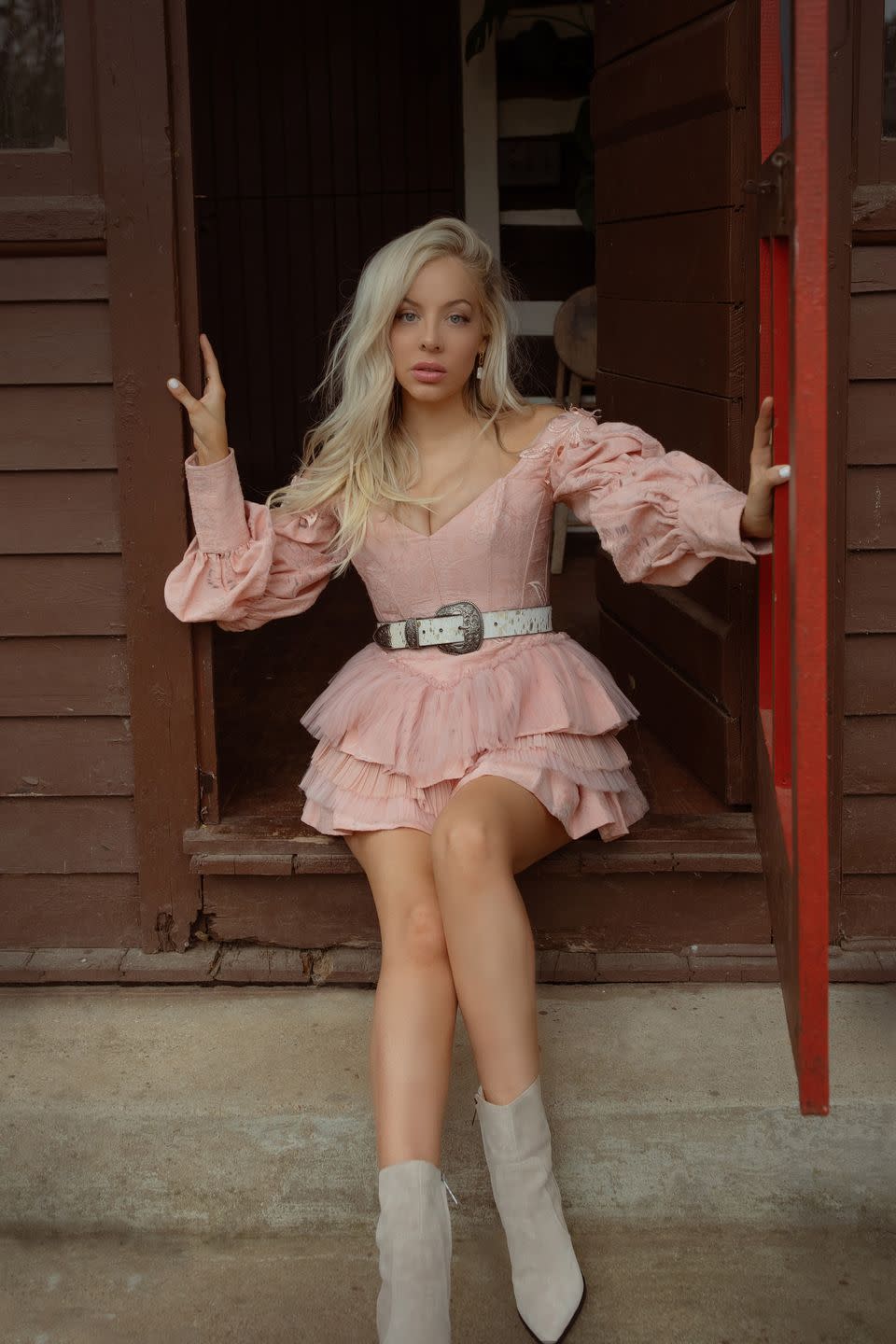 country singer songwriter mackenzie porter as an adult in pink western style dress, sitting on stoop of farmhouse