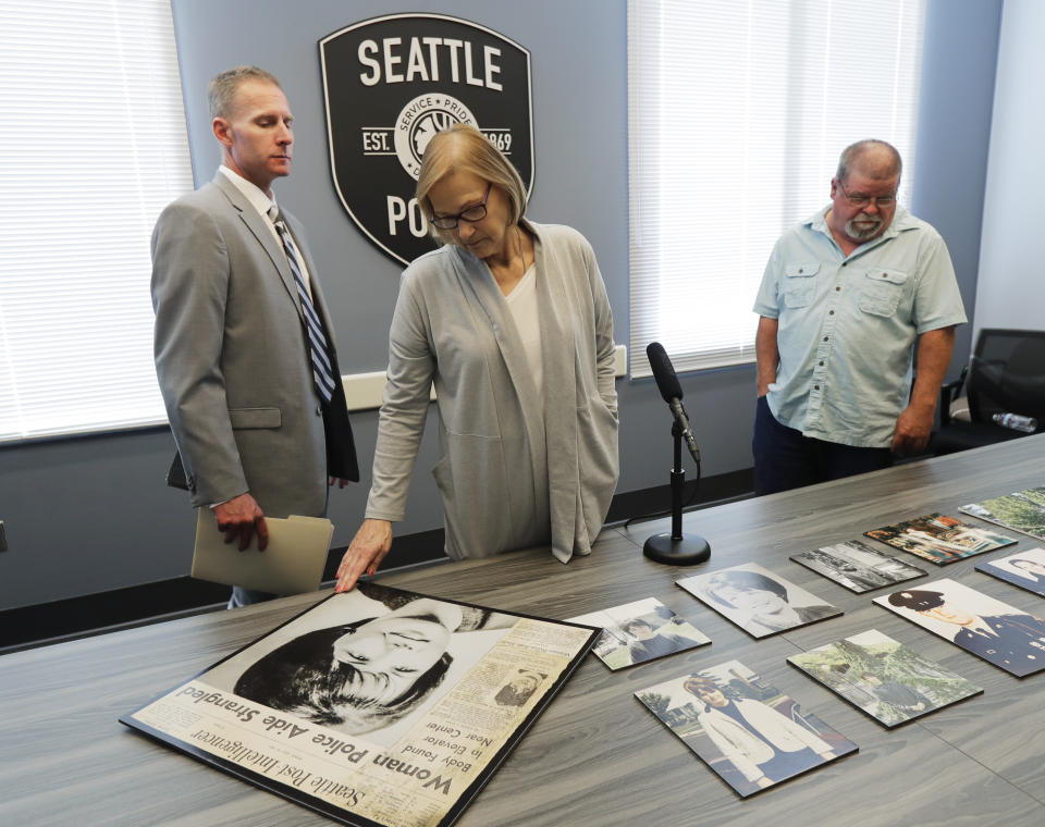 Kathy Galvin, center, looks at a photo of Susan Galvin, who was murdered in Seattle in 1967 and was the sister of Kathy's husband Chris, right, at Seattle Police headquarters Tuesday, May 7, 2019, in Seattle. Seattle police said Tuesday they have solved the cold case of the murder of Susan Galvin - through the work SPD homicide Detective Rolf Norton, left - using DNA and a family tree - a method that has revolutionized cold-case investigations across the U.S. (AP Photo/Ted S. Warren)