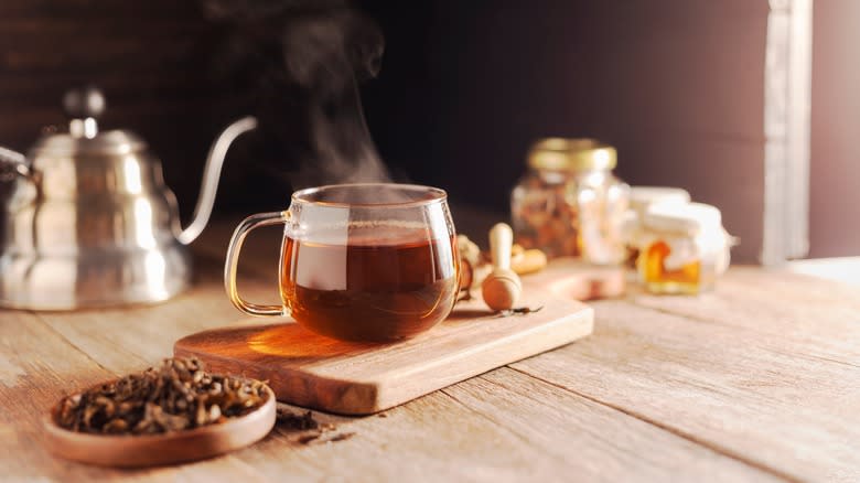 warm glass mug with tea and tea leaves nearby