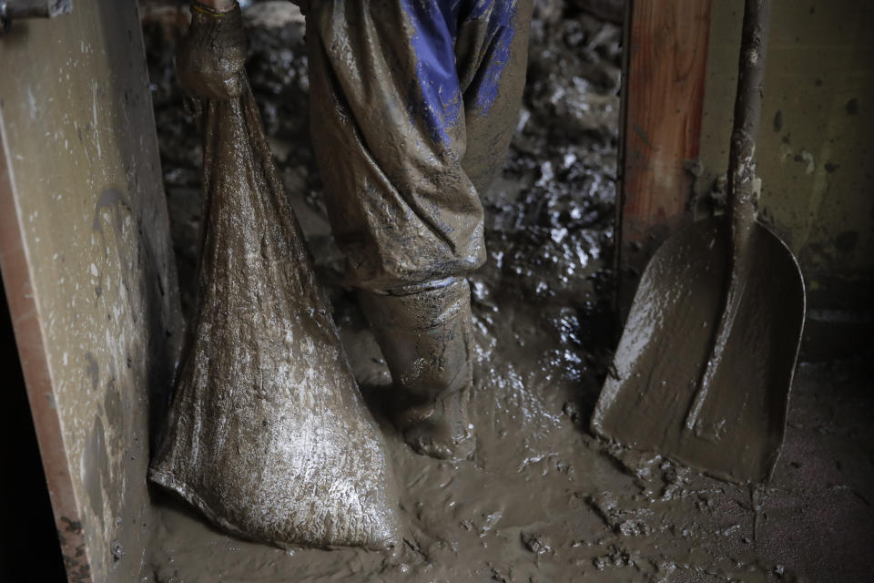 Masataka Murata carries a bag full of mud while cleaning up his friend's home damaged by Typhoon Hagibis Tuesday, Oct. 15, 2019, in Nagano, Japan. More victims and more damage have been found in typhoon-hit areas of central and northern Japan, where rescue crews are searching for people still missing. (AP Photo/Jae C. Hong)