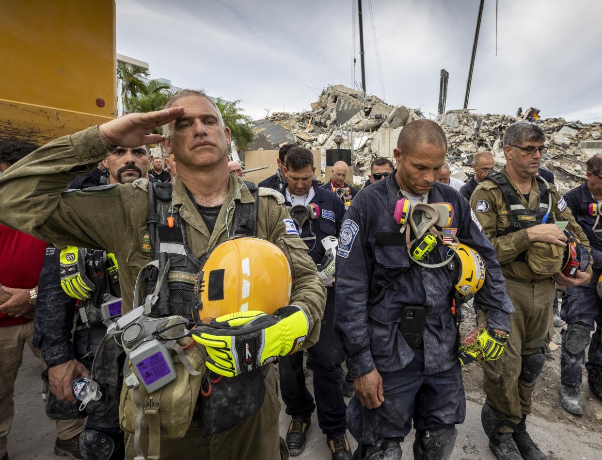 A member of the Israeli search and rescue team, left, salutes in front of the rubble that once was Champlain Towers South during a prayer ceremony on Wednesday, July 7, 2021, in Surfside, Fla. Members of search and rescue teams and Miami-Dade Fire Rescue, along with police and workers who have been working at the site of the collapse gathered for a moment of prayer and silence next to the collapsed tower.