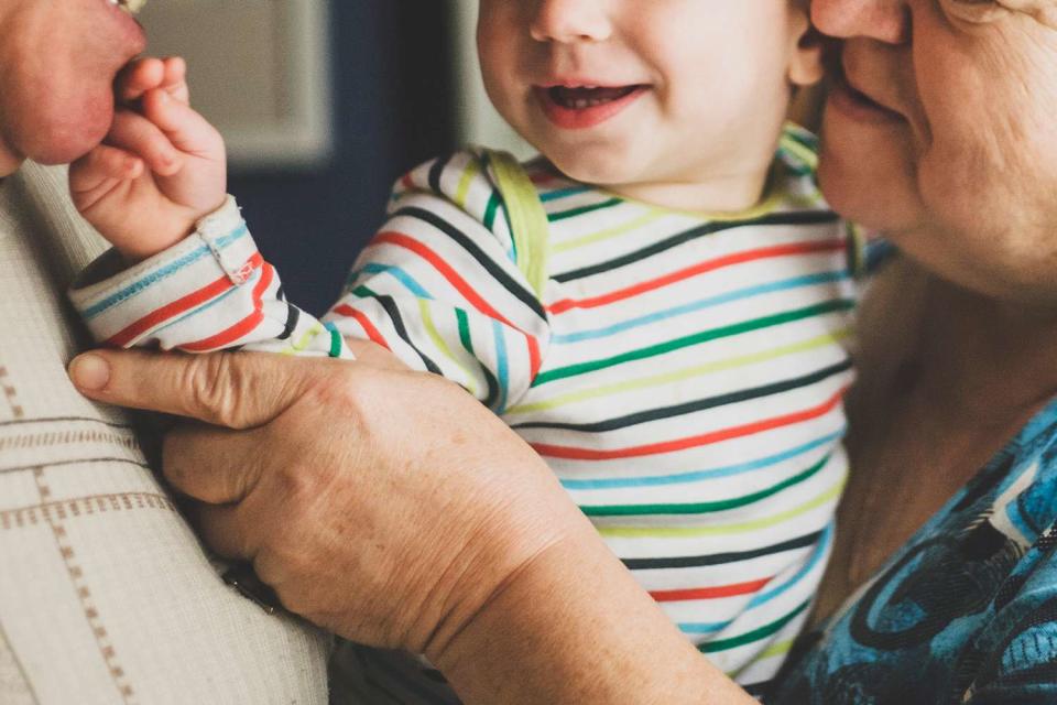 <p>Westend61/Getty</p> Happy grandparents holding their baby grandchild in a stock photo